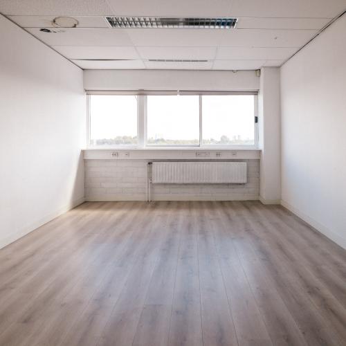 Lege, lichte kamer met een houten vloer en een groot raam met radiateur.