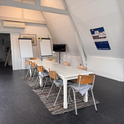 Medium ruimte Taalhuis: lange tafel met stoelen eromheen, twee whiteboards en een poster aan de muur