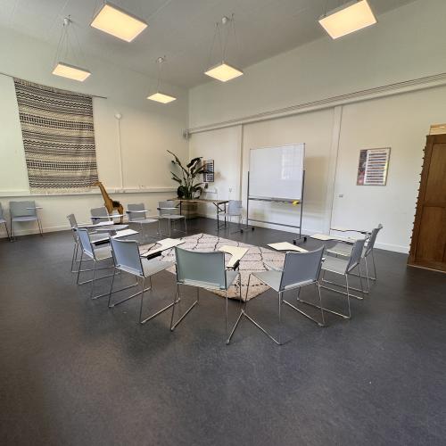 Taalhuis Amsterdam grote ruimte: stoelen met klaptafels in een kring, whiteboard, archiefkast.