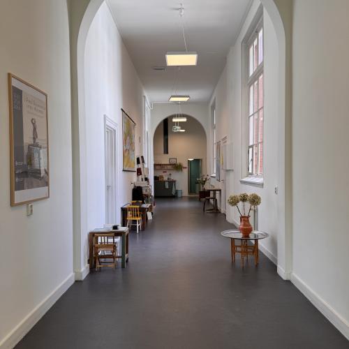 Taalhuis Amsterdam hal: hoge hal met rondboog, kleine tafeltjes langs de wand. Posters aan de muur.