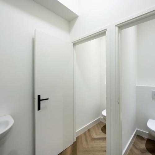 Interieurfoto van een badkamer met een wastafel, witte deur en een toilet in de achtergrond.