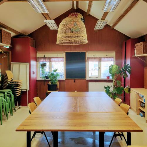 Grote, houten vergaderzaal met een lange tafel en lichte, slanke meubels onder een zolderdak.