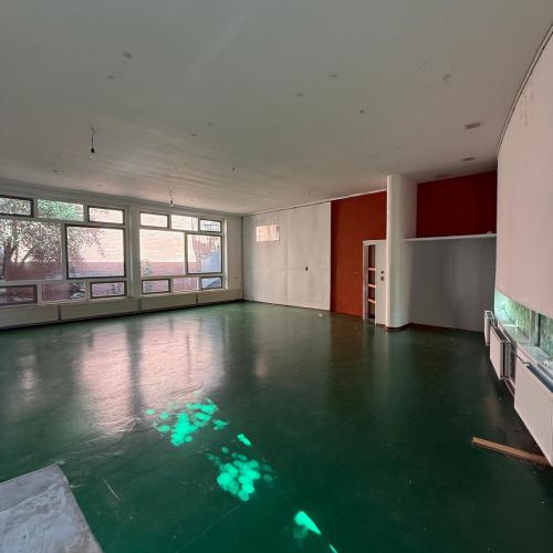 Leeg, modern interieur met een glanzende, donkergroene vloer. Grote ramen zorgen voor sterk reflecterend natuurlijk licht.