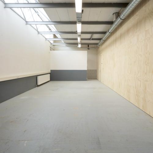 Leeg, industrieel ruim met grijze vloer, wit plafond, en een grote, lichtgekleurde muur.