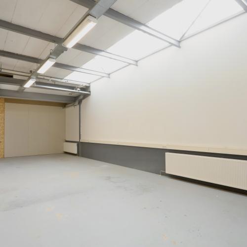 Leeg, ruim interieur met zichtbare constructie, witte muren, een betonvloer en een radiator langs de muur.