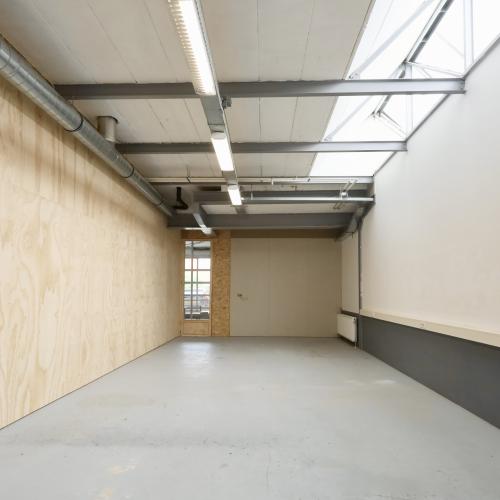 Grote, leegstaande kamer met houten wanden, wit plafond, en dakraam.
