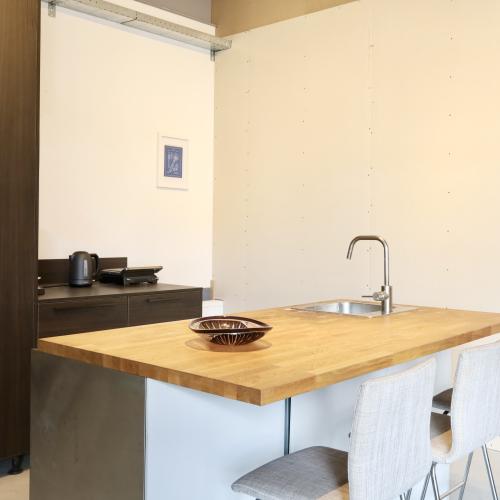 Keukenopstelling met houten aanrechtblad, wasbak en rij witte stoelen.