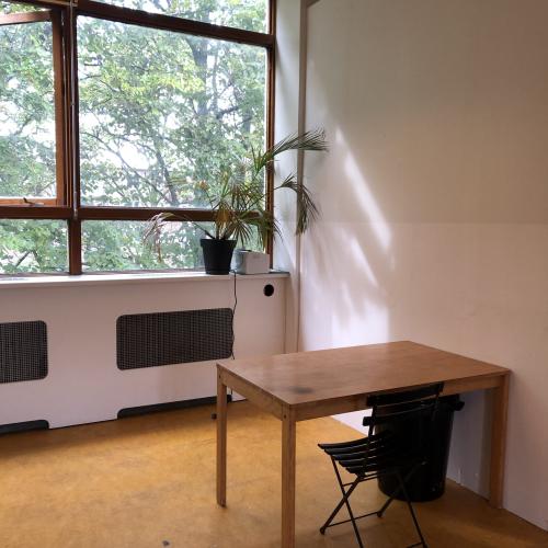 Zaal met groot raam, licht en een eenvoudig, houten bureau met een zwarte stoel.