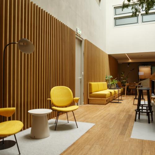 Interieur van een moderne lounge: felgele stoelen voor een verticale houten wand, en een houten bargebied rechts.