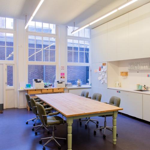 Taalhuis keuken: een grote tafel et stoelen rondom. Lang aanrecht, afwasmachine en glazen op plank. 