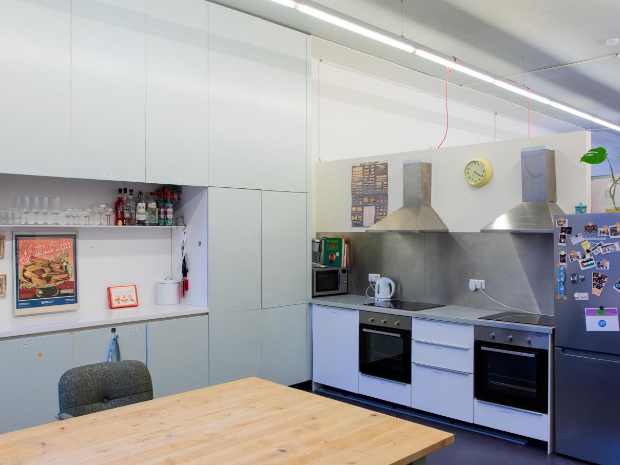 Taalhuis Keuken: Een grote tafel, 2 inductiekookplaten, 2 ovens en afzuigkap, koelkast en aanrecht.