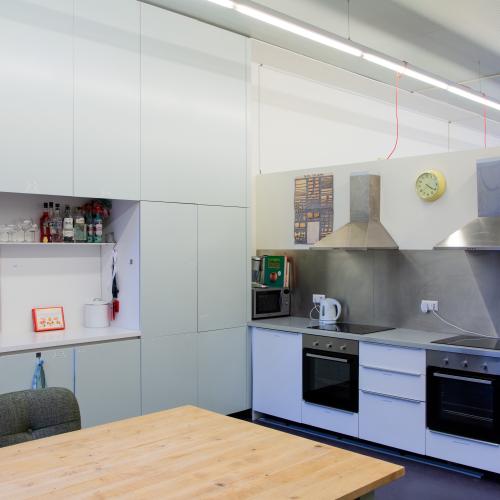 Taalhuis Keuken: Een grote tafel, 2 inductiekookplaten, 2 ovens en afzuigkap, koelkast en aanrecht.