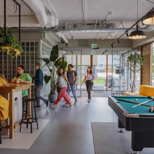 Moderne lounge met pooltafel en bar. Een groep mensen loopt door de lichte, sociale ruimte.