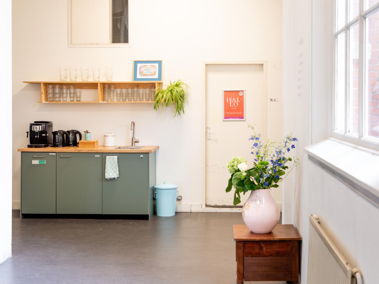 Ruime hal en een kitchenette met koffie/thee en een kraan. Vaas met bloemen in de hal.