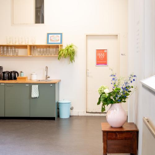 Ruime hal en een kitchenette met koffie/thee en een kraan. Vaas met bloemen in de hal.