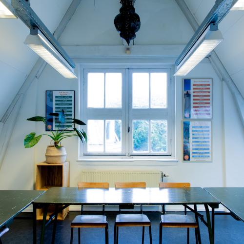 Lange vergaderruimte met slanke tafels en stoelen, badend in daglicht door een dakraam.
