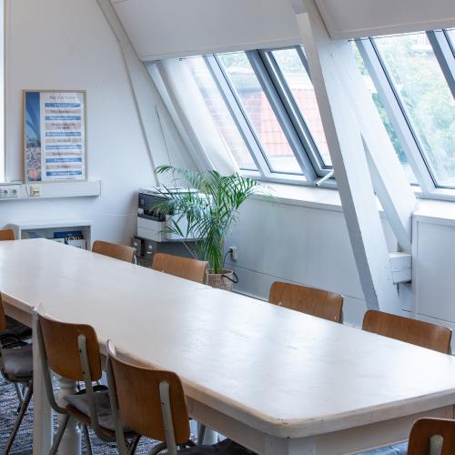 Grote, lange vergadertafel met stoelen in een lichte ruimte met dakramen.