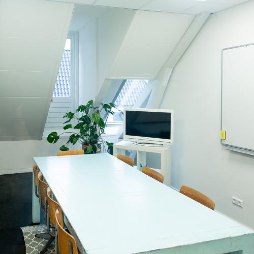 Grote, moderne vergaderzaal met een lange tafel, stoelen, een projectiescherm en een bord.