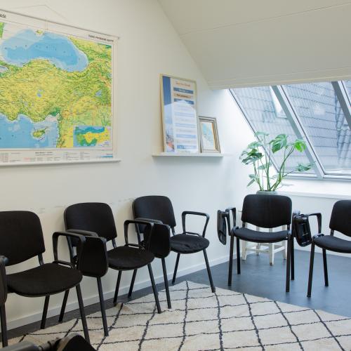 Een lichte vergaderzaal met rijen zwarte stoelen, een groot geografisch kaart en een modern raam met veel lichtinval.