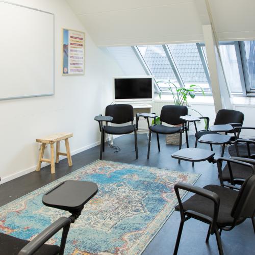 Zakelijke vergaderruimte met een wit bord, diverse stoelen en een zacht tapijt.