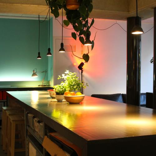 Moderne bar met donker blad. De ruimte heeft tealtgroene en witte muren, versierd met hangplanten en warme spotverlichting.