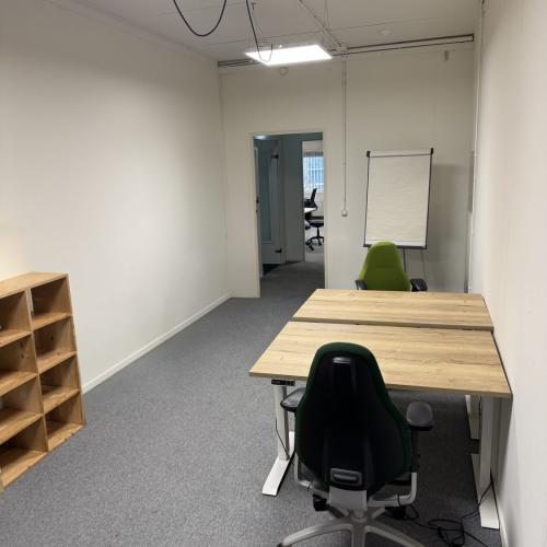 Vergaderruimte met een lichte tafel, bureaustoel en een houten plankkast. Op de achtermuur staat een whiteboard.