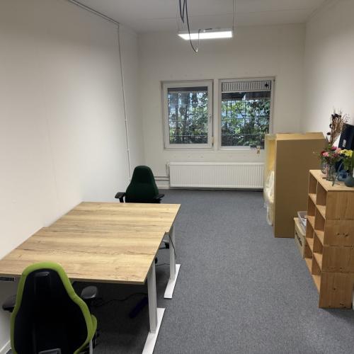 Kantoorruimte met licht houten bureau, groene stoel en opgeslagen objecten.