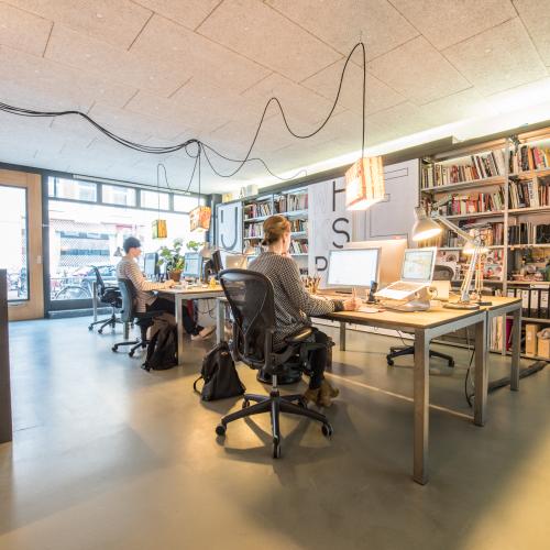 Een modern kantoor met open werkplekken. Mensen werken aan bureaus naast grote boekenplanken.