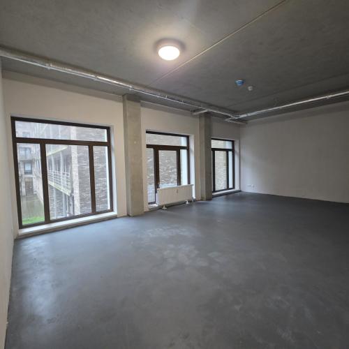 Groot, leeg interieur met donker betonvloer, hoge ramen en strak wit plafond.