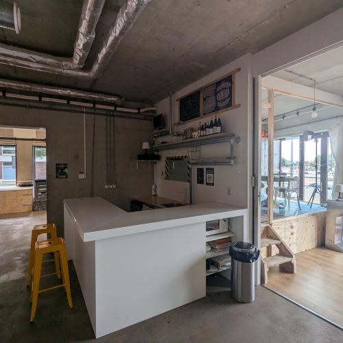 Modern, industrieel interieur met een witte balie en veel natuurlijk licht vanuit grote ramen en glazen deuren.
