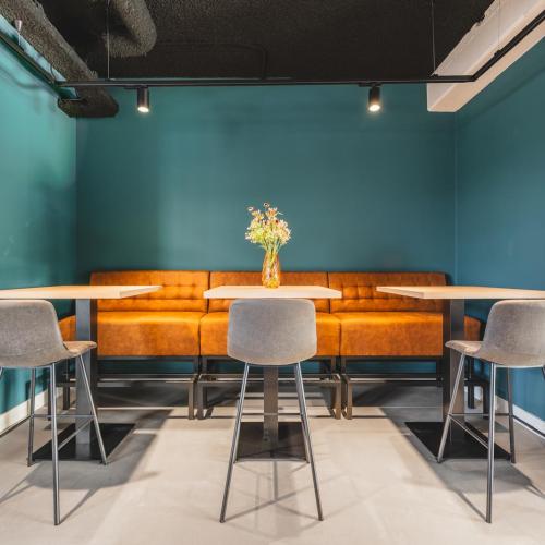 Interieurfoto van een trendy cafégedeelte met een oranje bank, drie kleine tafels en stoelen.