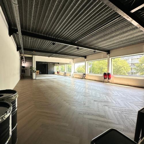 Grote, moderne hal met een industrieel metalen plafond, lichte vloer en grote raampartijen met uitzicht op groen.
