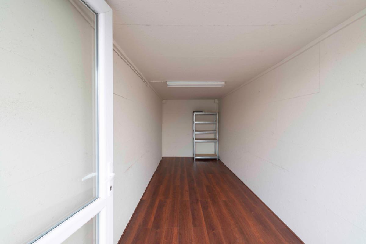 Lege, moderne hal met een donkere houten vloer, witte muren en een rek in de verte.