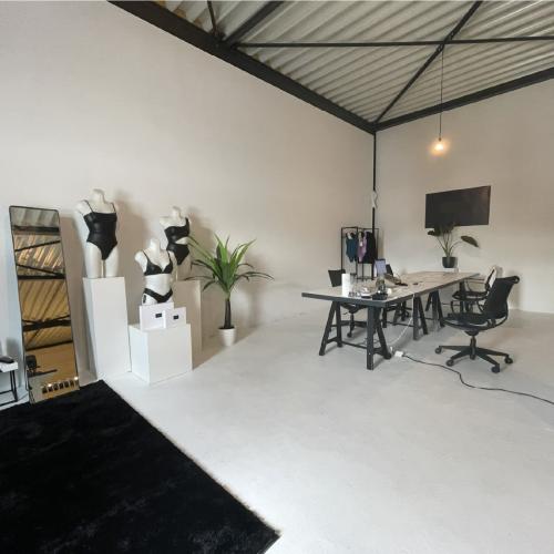 Ruime, lichte werkruimte met industrieel plafond. Links decorstukken, rechts een kantoordesk en monitor opgesteld.