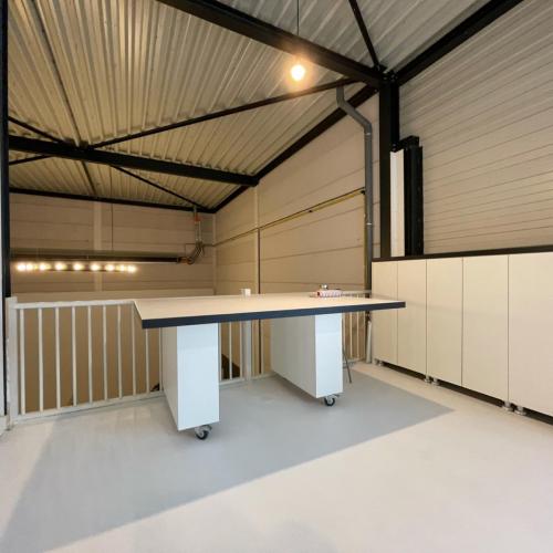 Modern kantoorinterieur: grote tafel in een industriële loods met witte kasten en stalen constructie.