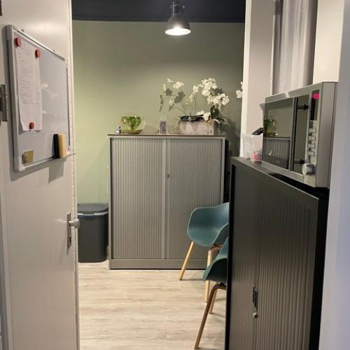 Interieur van een moderne kamer met grijs kastenwerk, een tealtel stoel, een bloemstuk en een prikbord.