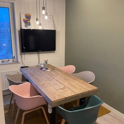 Houten eettafel met verschillende kleurrijke stoelen (roze en blauw) in een moderne, lichte eetkamer.
