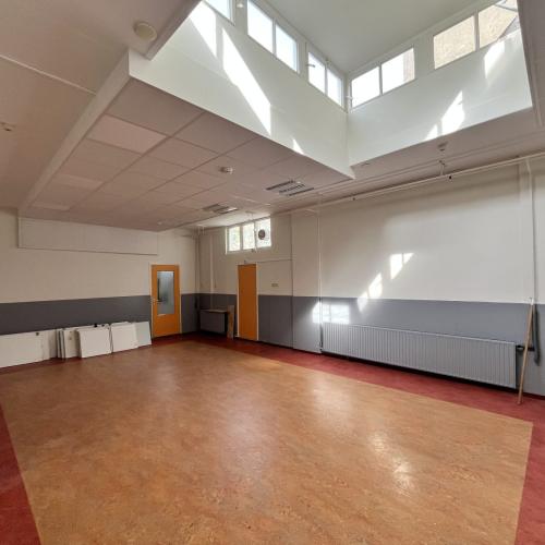 Grote, lege vergaderzaal met lichte muurpanelen en grote dakramen.