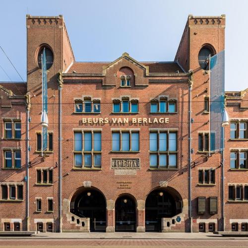 Historisch gebouw met bakstenen façade, de Beurs van Berlage, afgebeeld tegen een helderblauwe lucht.