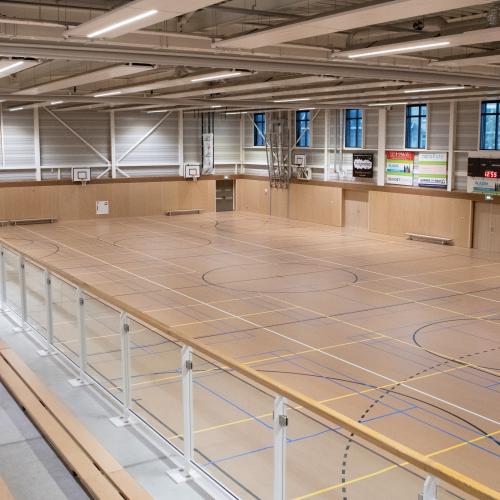 Overzicht van een lege, lichte indoor sportzaal met houten vloer en informatiebalies.